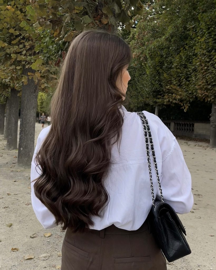Back view of long wavy deep chestnut brunette hair worn loose while walking outdoors, a low-maintenance fall brunette hair color.