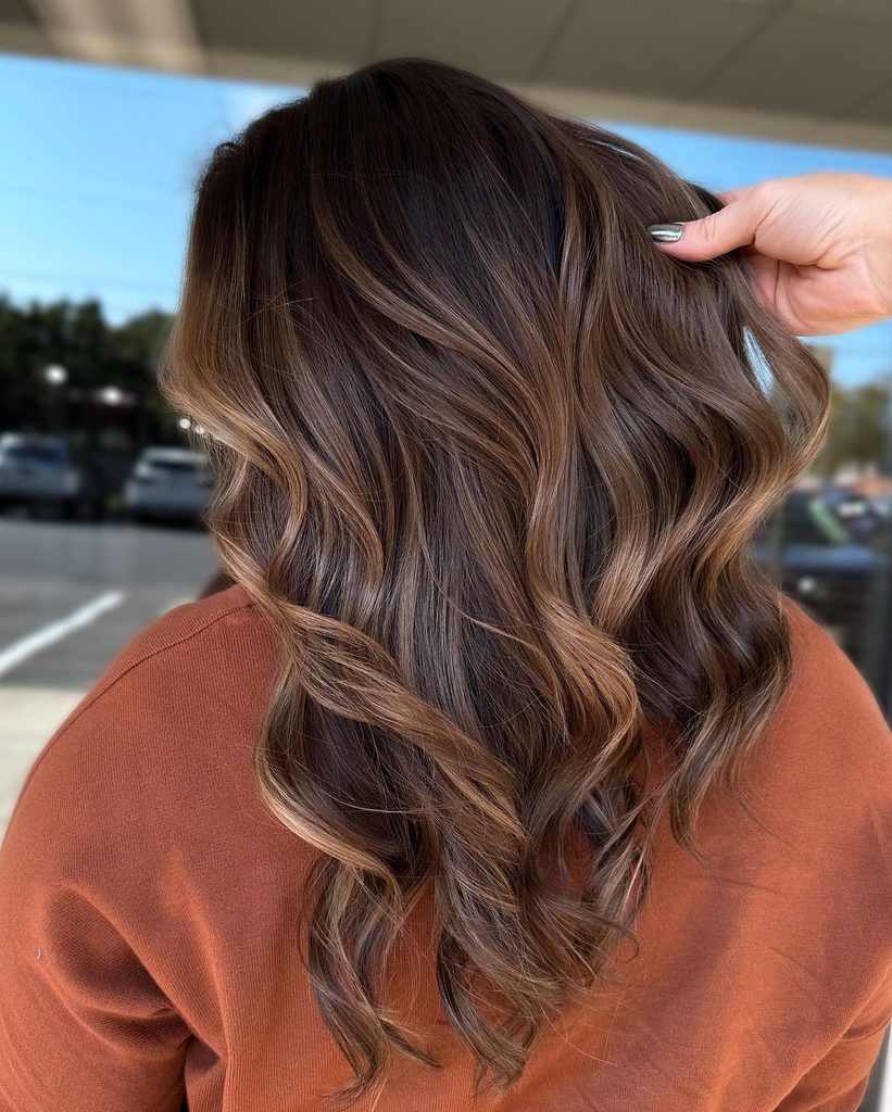 Back view of brunette hair with honey gloss balayage and soft curls, worn with a burnt orange sweater for a classic fall hair color pairing.