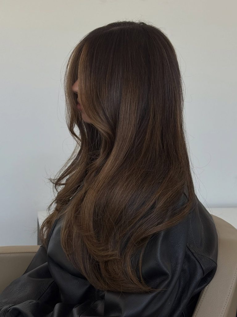 Side profile of long wavy rich espresso brunette hair with subtle caramel highlights, a deep dark fall hair color.