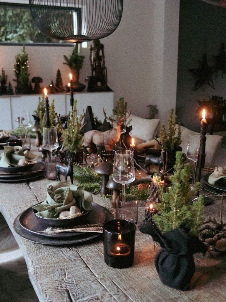 Moody Christmas table decor with black candles, mini trees in dark pots, and sage linen napkins
