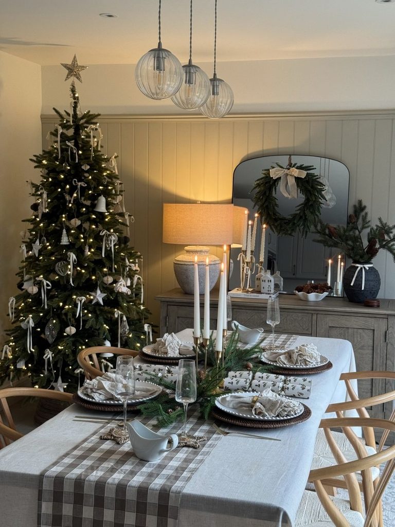 Christmas dining table with a gingham runner, candles, and greenery in front of a decorated tree