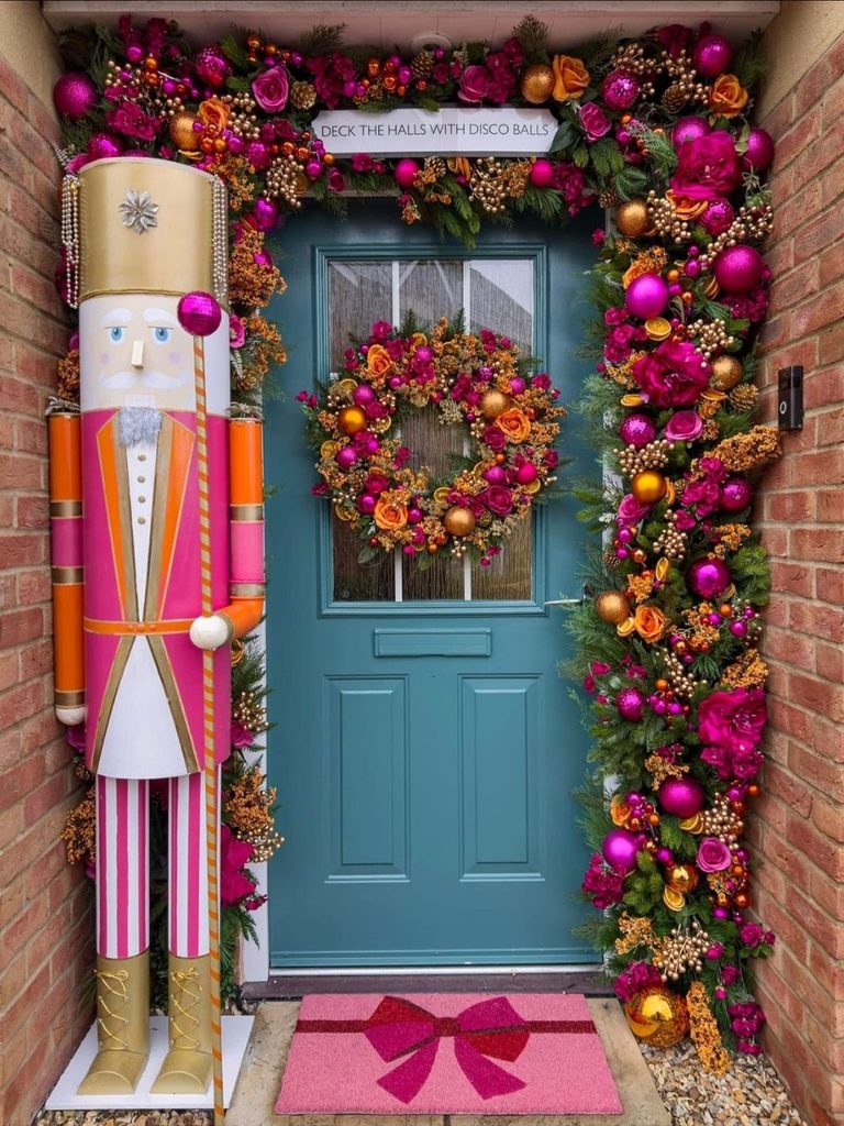 Giant pink and gold nutcracker beside a teal front door framed in magenta and orange Christmas decor ideas garland.