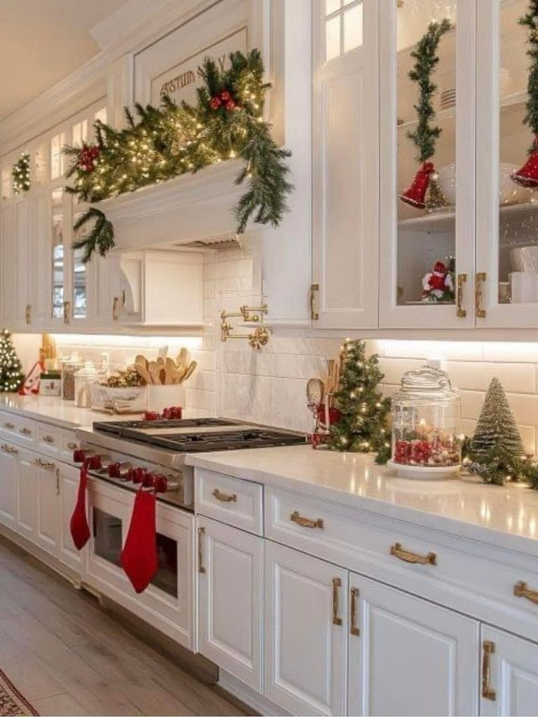 White Christmas kitchen decor with garland over the range hood, red stockings by the stove, and mini trees on the counter