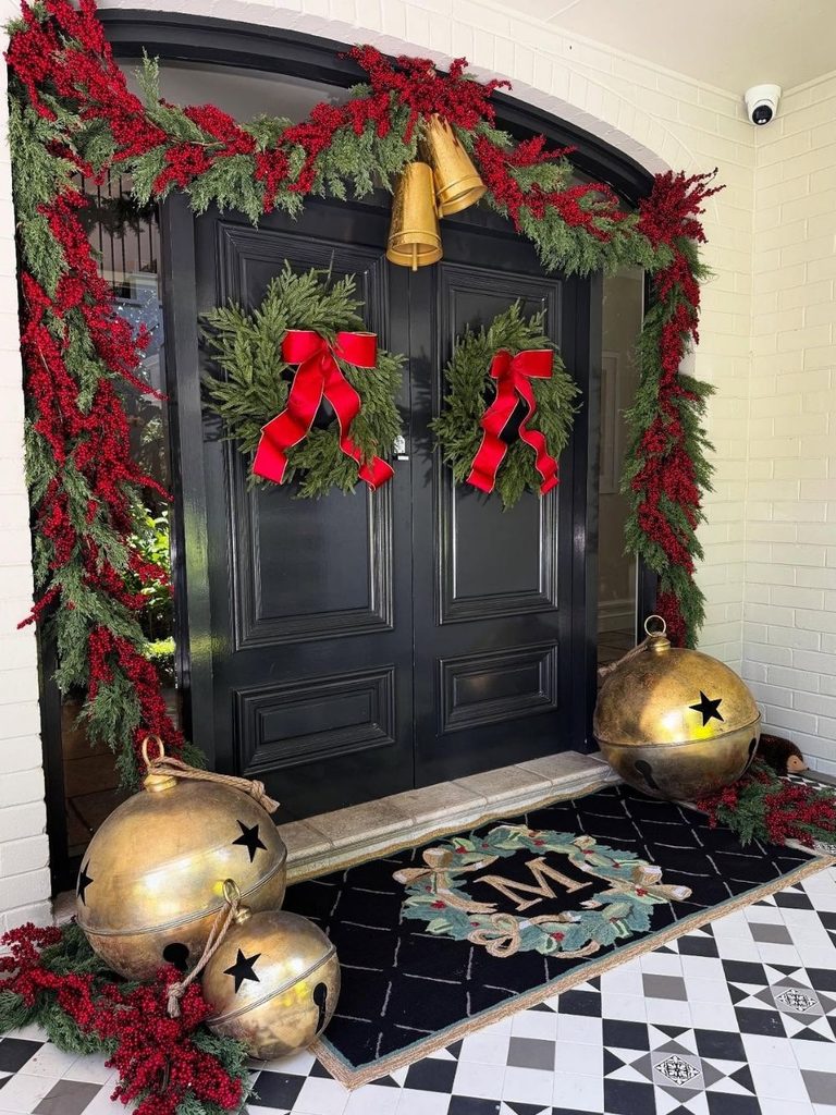 Black double doors framed with red berry garland, red bow wreaths, and giant gold jingle bells
