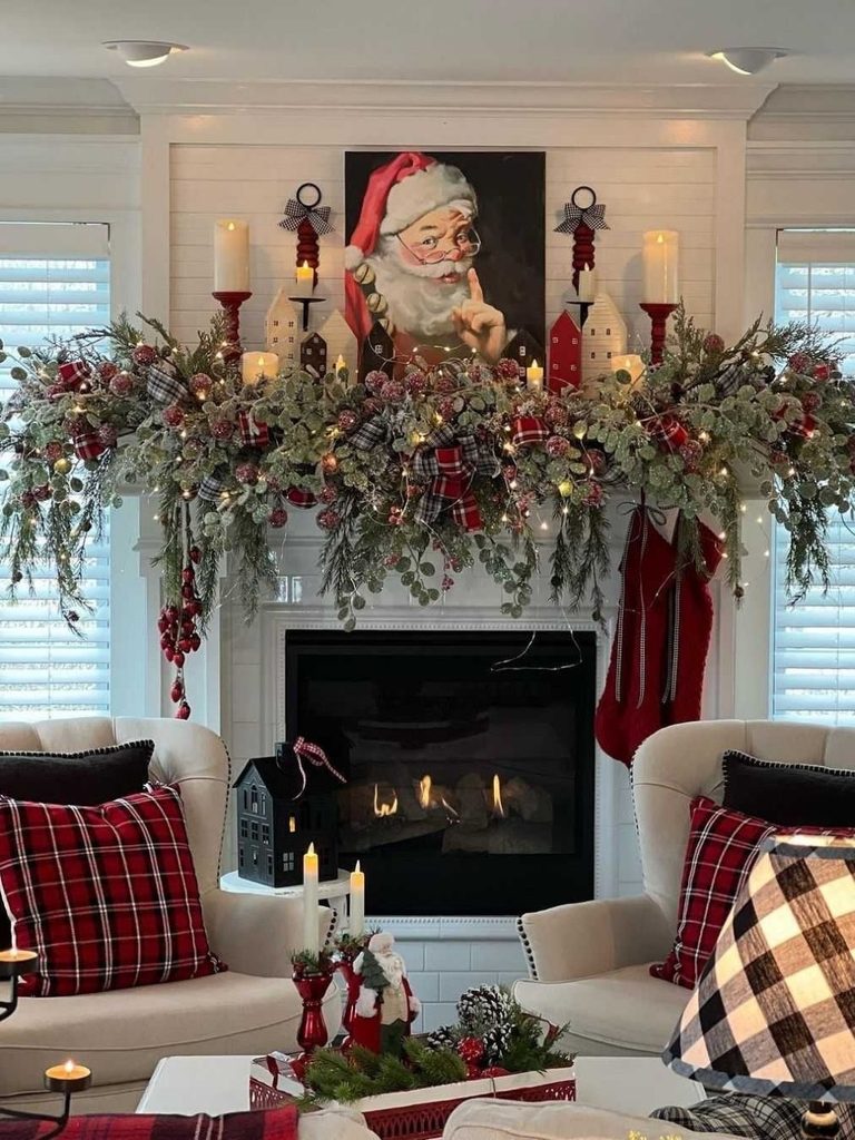 Fireplace mantel with a vintage Santa portrait, lush garland, red candles, and buffalo plaid pillows