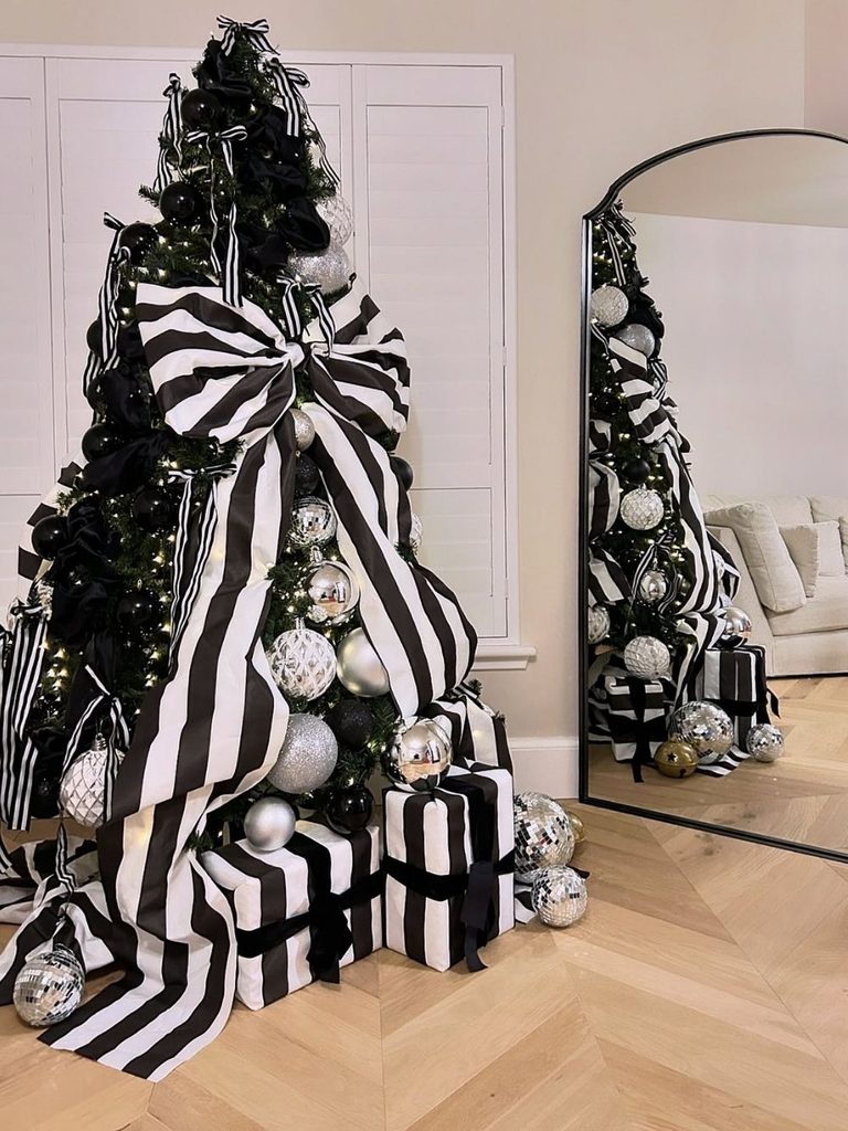 Black Christmas tree with oversized black and white striped ribbon, silver ornaments, and striped gift boxes