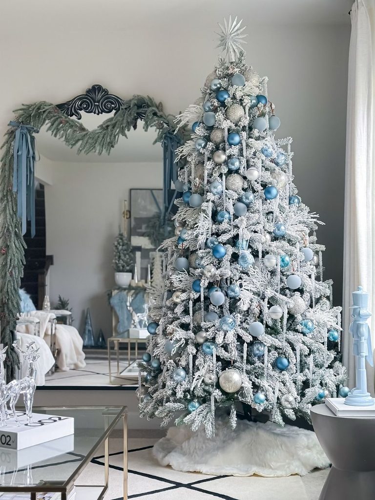 Flocked Christmas tree decorated in blue and silver ornaments in front of an arched mirror