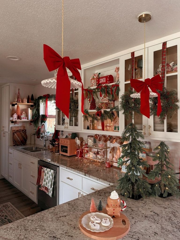 Christmas kitchen decor with giant red velvet bows hanging from the ceiling, wreaths on glass cabinets, and mini trees