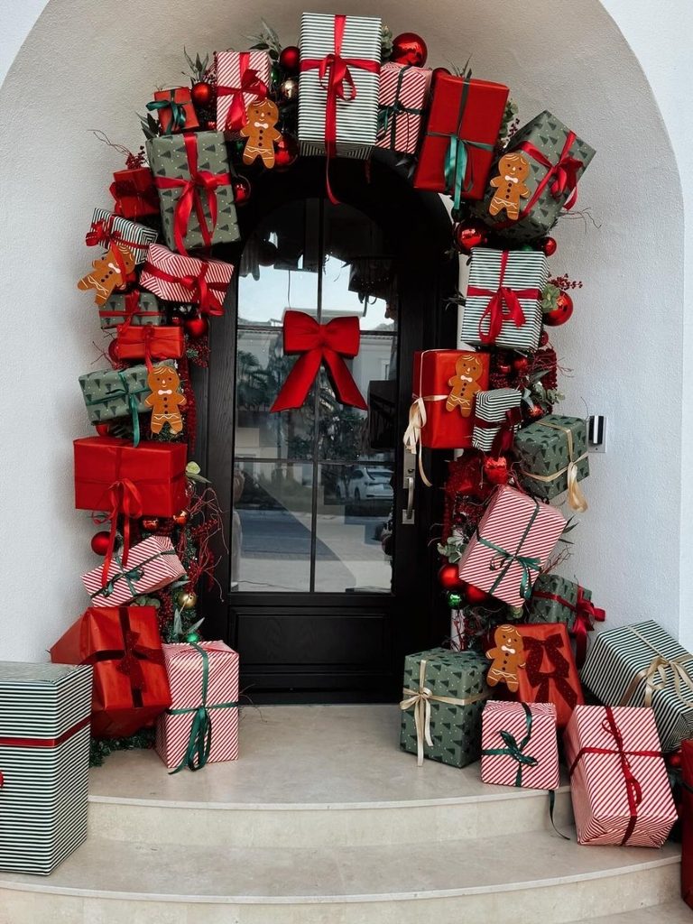 Arched entryway covered in red, pink, and green wrapped presents with gingerbread cookies and bows