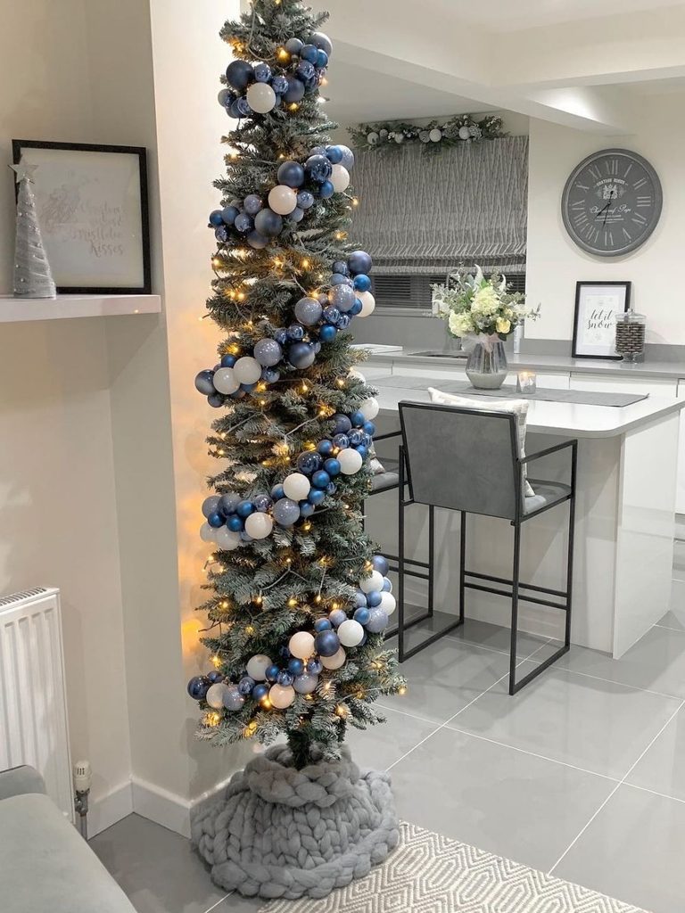 Slim pencil Christmas tree with blue and silver ornaments in a modern white kitchen