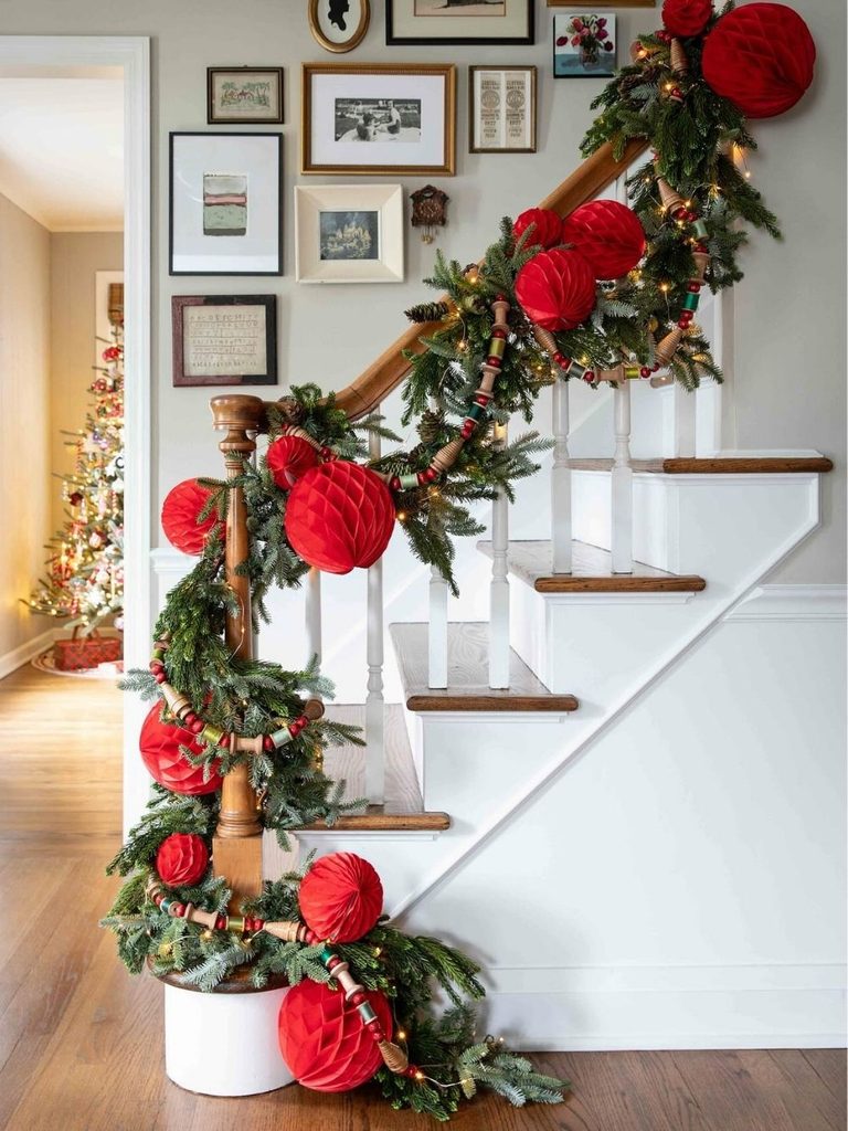 Christmas staircase decor with garland wrapped around the banister and big red pom pom accents