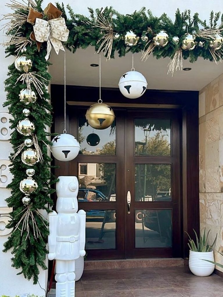 Dark front door framed in evergreen garland with gold and silver ornaments and a tall white nutcracker, outdoor Christmas decor