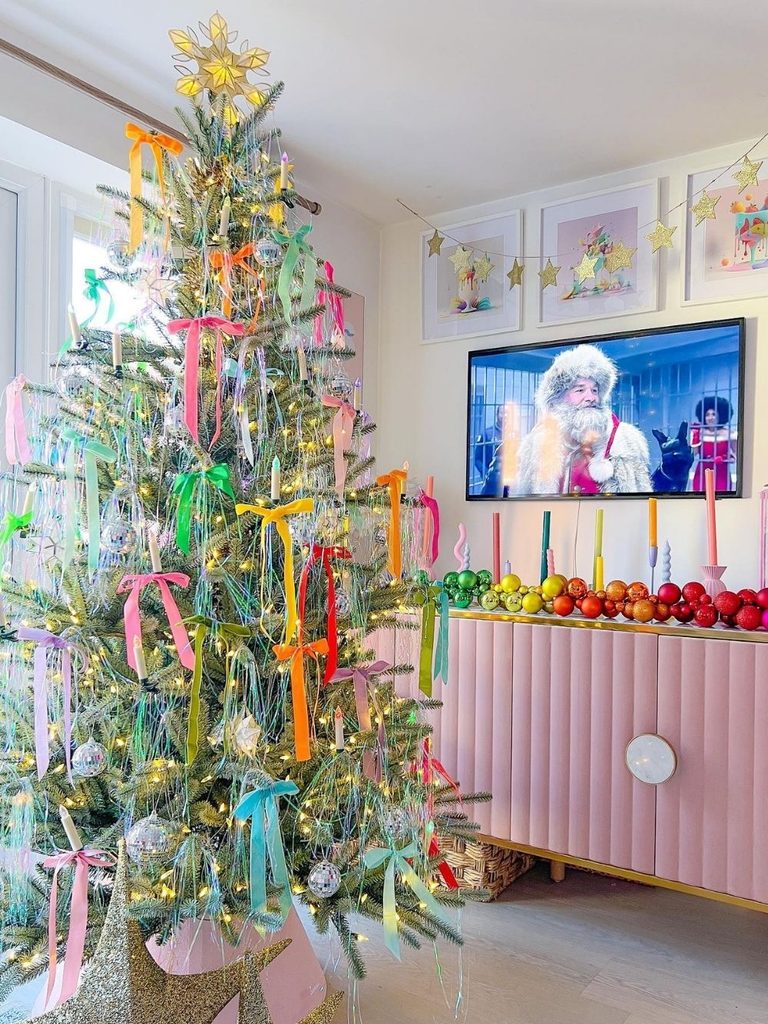 Christmas tree decorated with rainbow ribbon bows next to a pink fluted console and framed art
