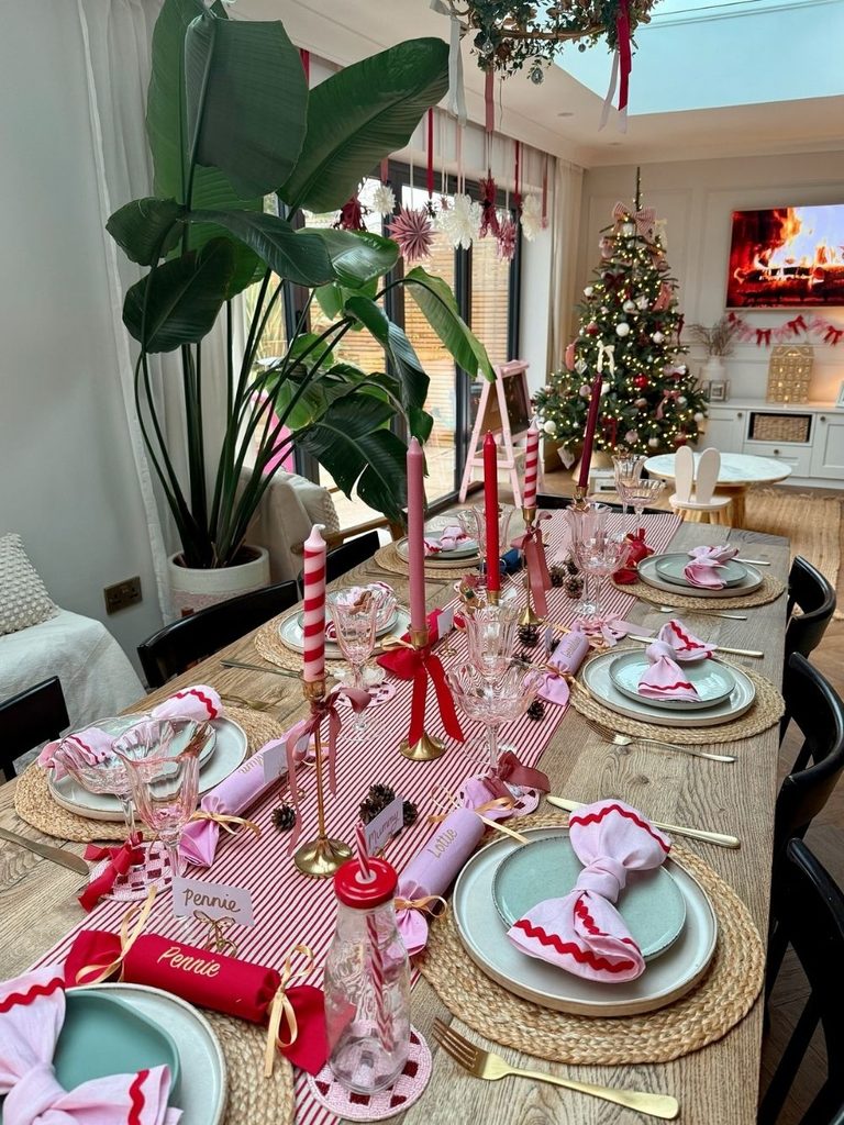 Long dining table with pink and teal plates, a striped runner, bows, and candy cane candles