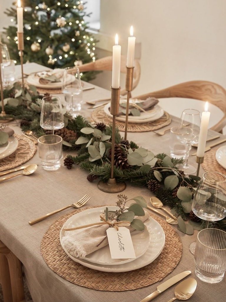 Christmas table decor ideas with woven placemats, brass taper candles, a eucalyptus runner, and handwritten place cards