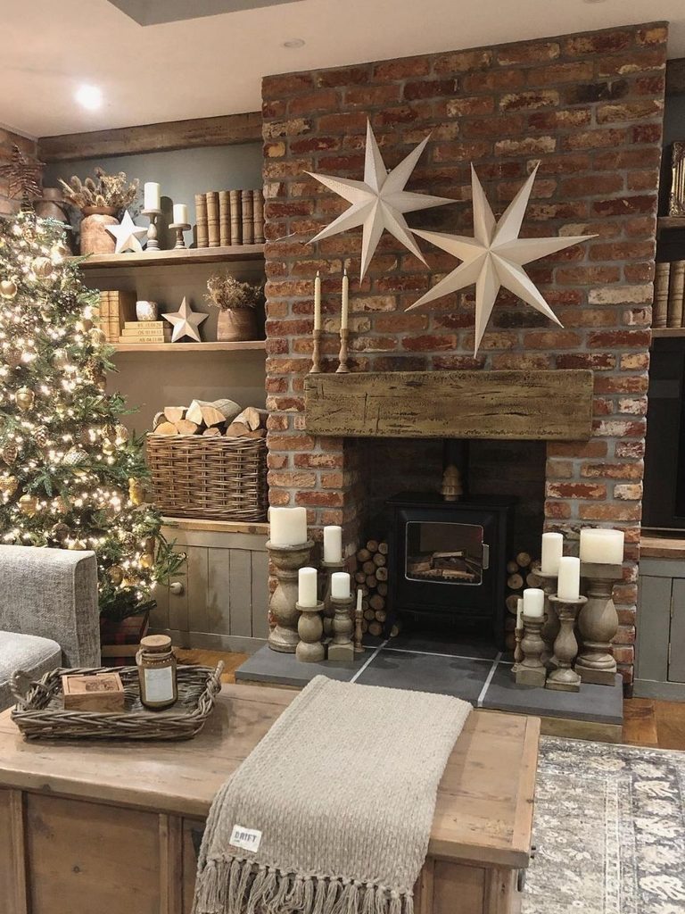 Living room Christmas decor ideas with two giant white paper stars above a brick fireplace, wooden candlesticks on the hearth, and a lit tree