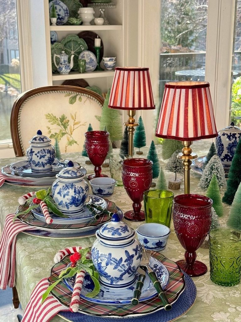 Christmas table with blue and white porcelain, striped lamp shades, red and green glasses, and mini trees