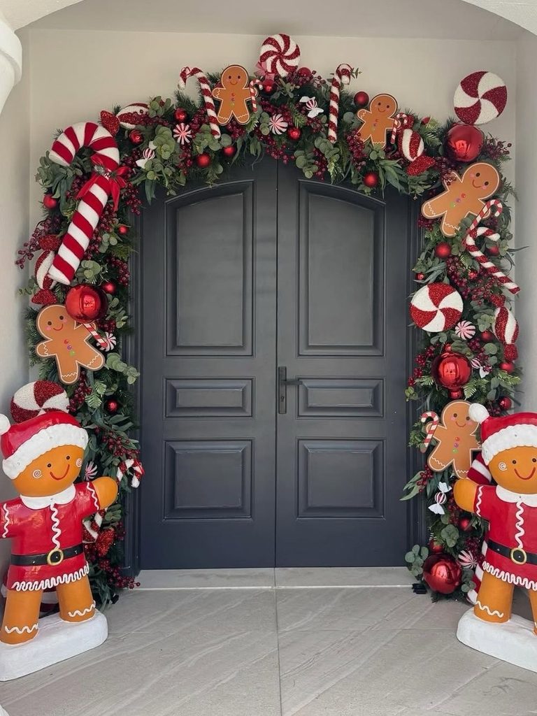 Gray double doors framed by a garland of candy canes, ornaments, and gingerbread cutouts with two gingerbread figures