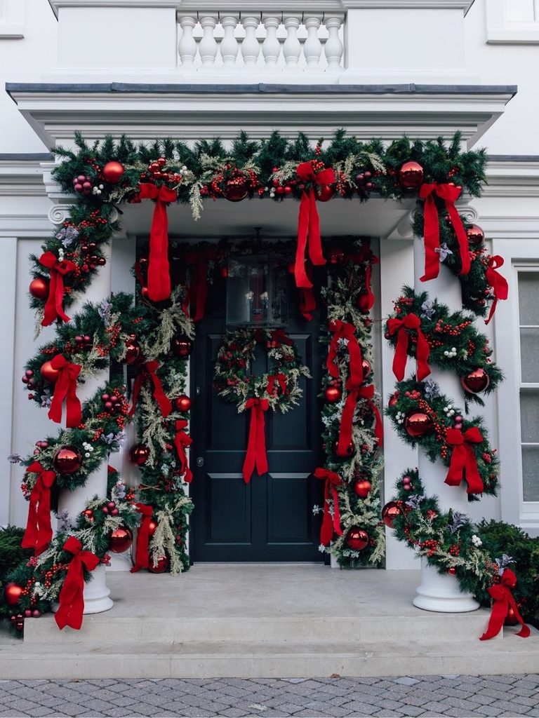 White house entrance with garland and cascading red velvet bows around a dark front door and wreath