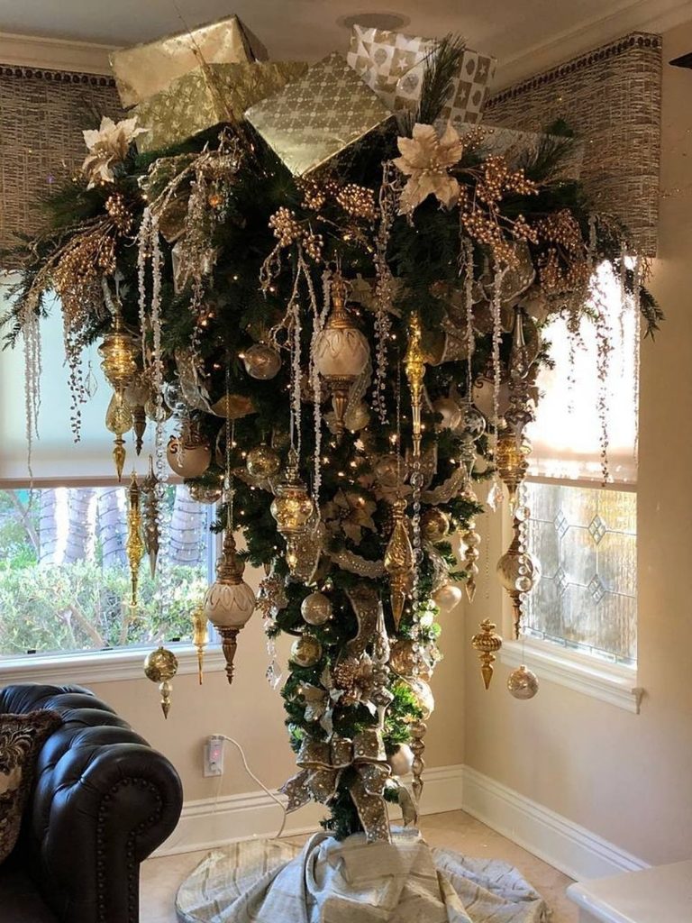 Upside-down Christmas tree hanging from the ceiling with gold ornaments and ribbon in a living room