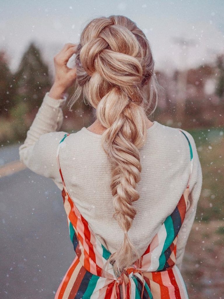 Loose, voluminous braided ponytail with face-framing wisps against a snowy backdrop