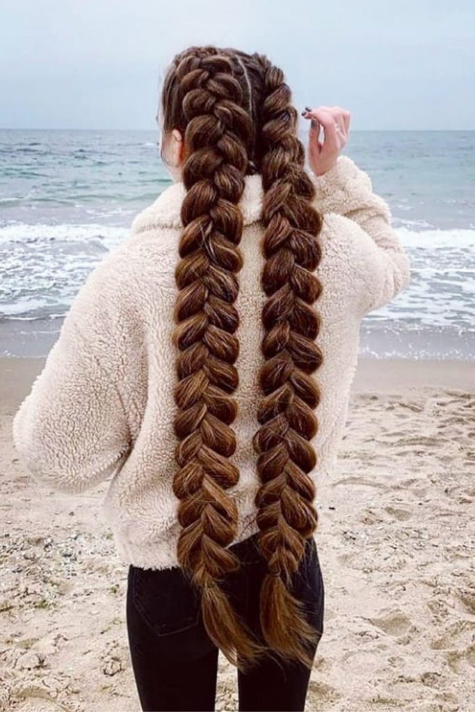 Chunky double Dutch pigtail braids on a beach in a fluffy white jacket