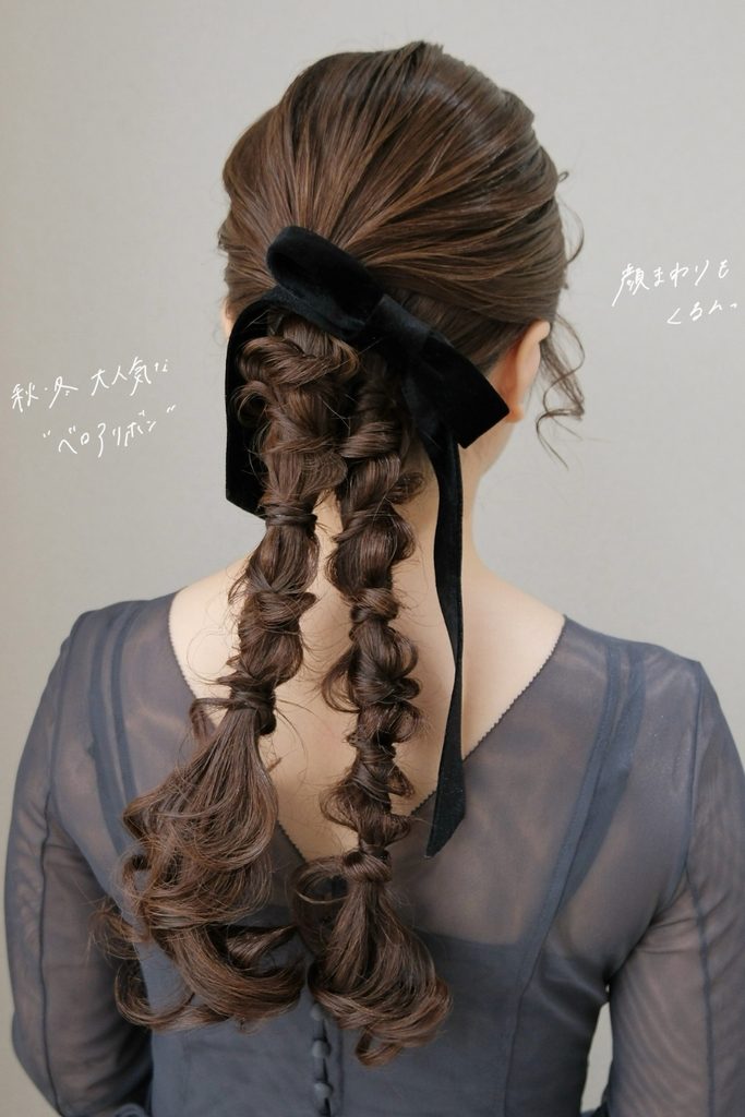 Low ponytail split into two textured braids with face-framing curls and a black velvet bow