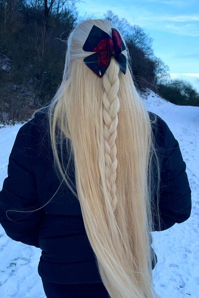 Half up half down hair with a thin braid down the center and a navy plaid bow in the snow
